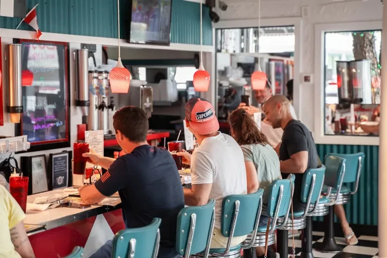 Interior of a retro diner with patrons at a red and white counter.