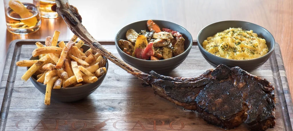Large seared Tomahawk steak with fries, roasted vegetables, mashed potatoes.