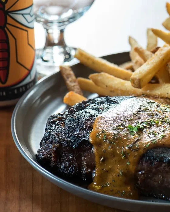 Char-grilled meat with creamy sauce, french fries, and a beer can.