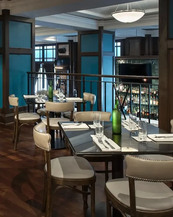 Modern restaurant interior with dark tables, light chairs, and bar.