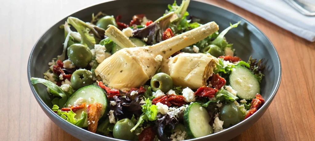 Fresh salad with artichoke hearts, olives, sun-dried tomatoes, feta, and lettuce.