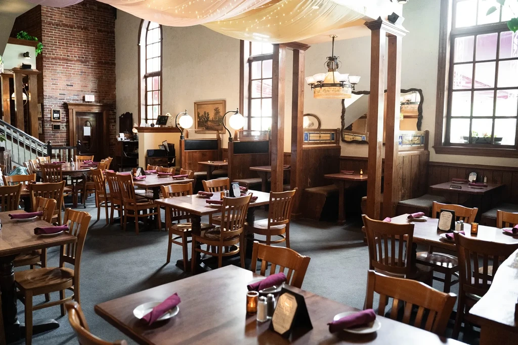 Empty rustic restaurant with wooden tables, brick walls, and draped string lights.