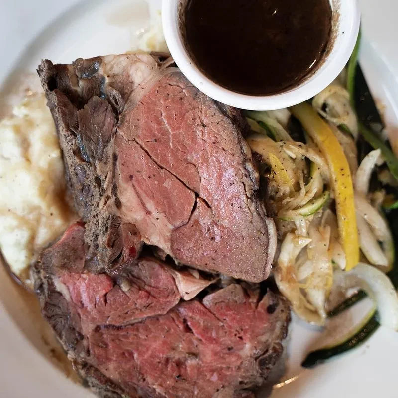 Plated medium-rare prime rib with mashed potatoes, sautéed vegetables, and gravy.