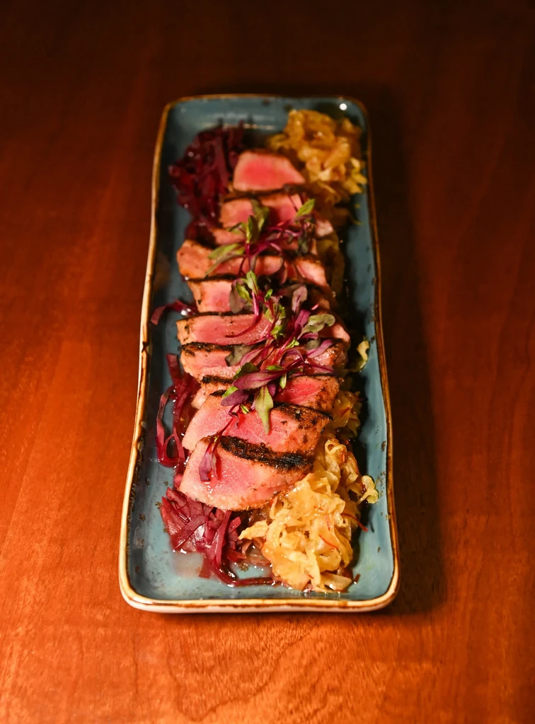 Medium-rare seared tuna, microgreens, pickled cabbage, and caramelized onions on plate.