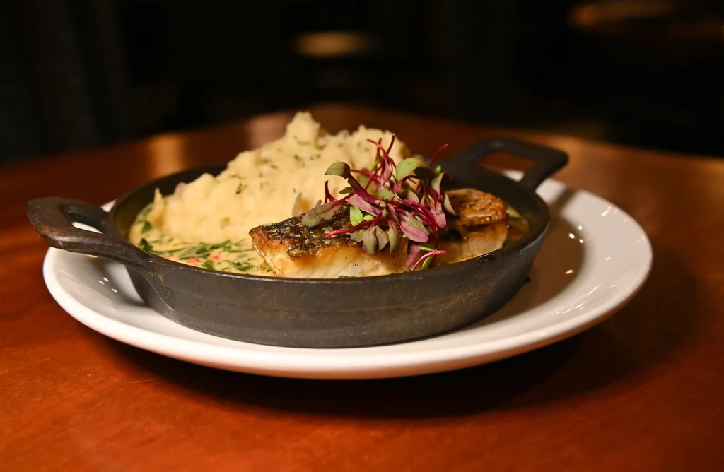 Pan-seared fish, microgreens, mashed potatoes, and sauce in a skillet.
