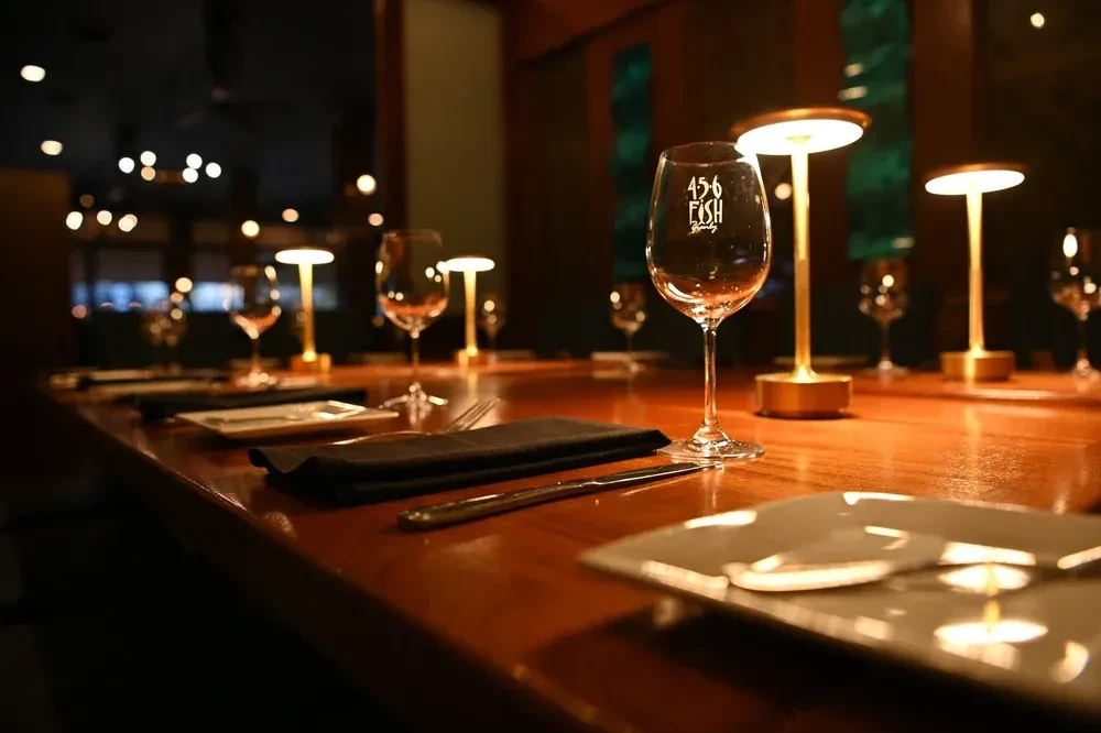 Wooden restaurant table set with lamps and '456 FISH Brewery' wine glasses.