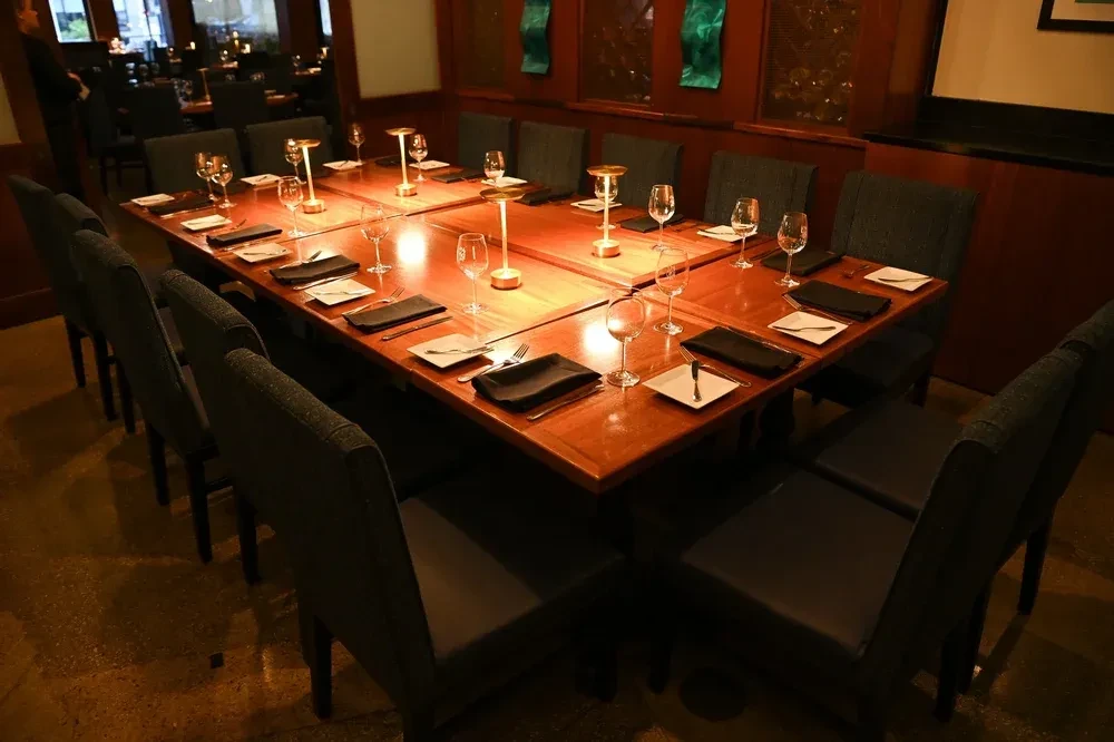 Polished wooden dining table set for 14 with warm lamps.