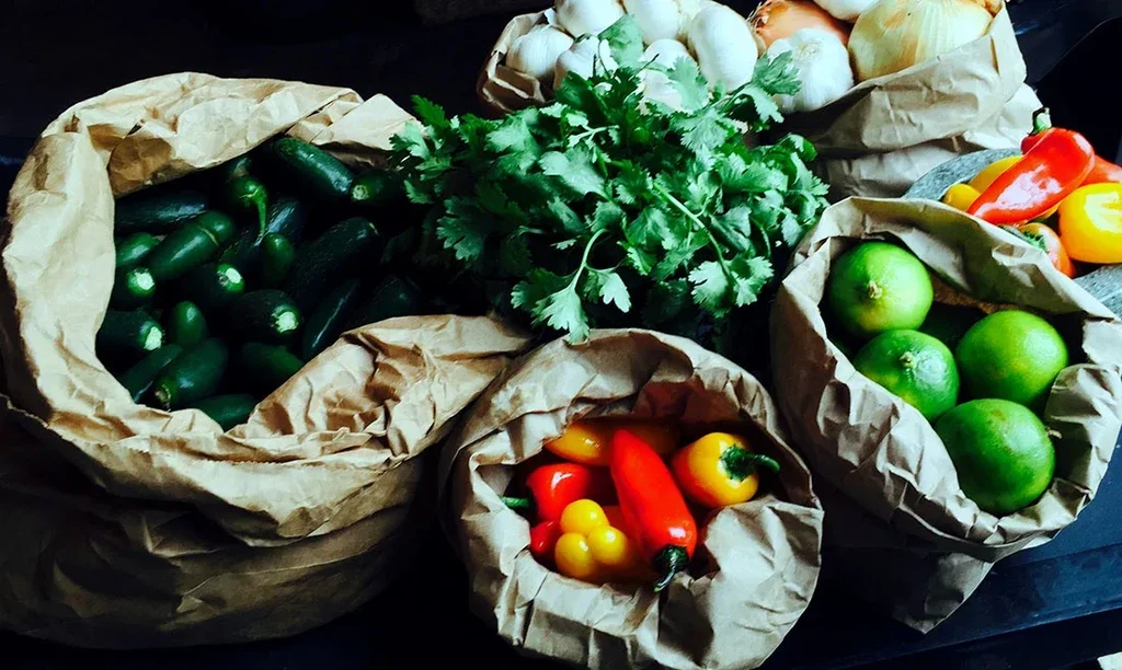 Assorted fresh produce in paper bags: jalapeños, cilantro, garlic, onions, limes.