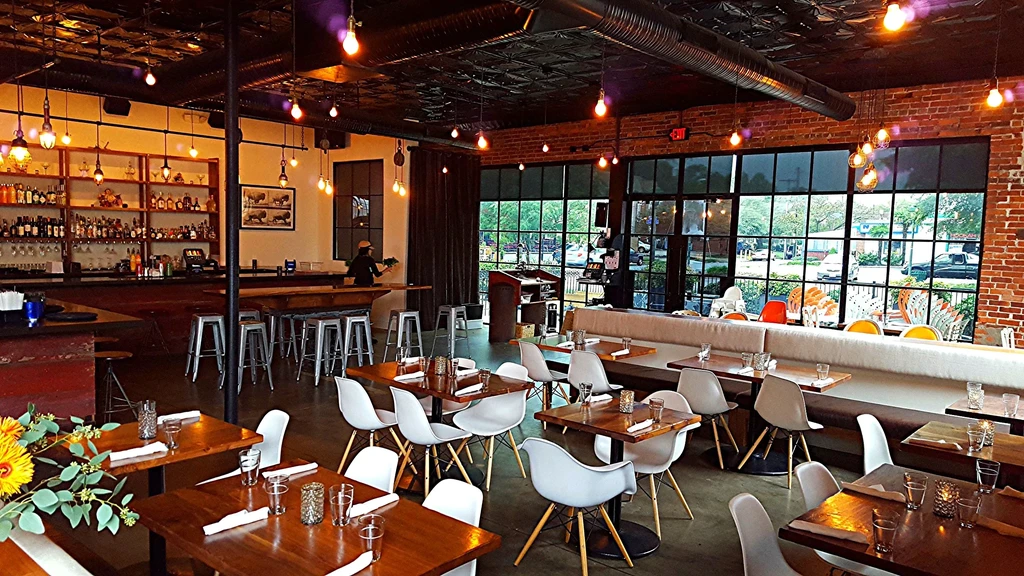 Modern restaurant interior with bar, dining tables, and warm industrial lighting.