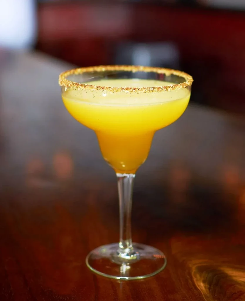 Yellow-orange margarita cocktail in a stemmed glass with a textured rim.
