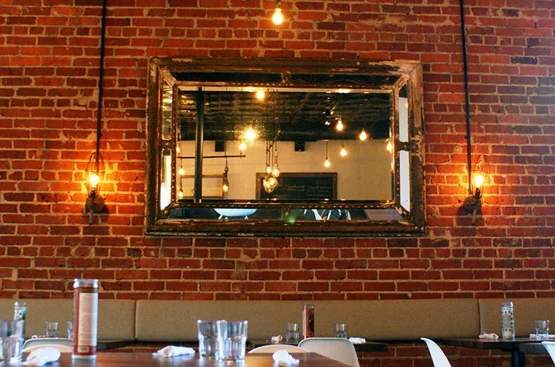Vintage mirror on brick wall reflects Edison bulbs, flanked by lights.