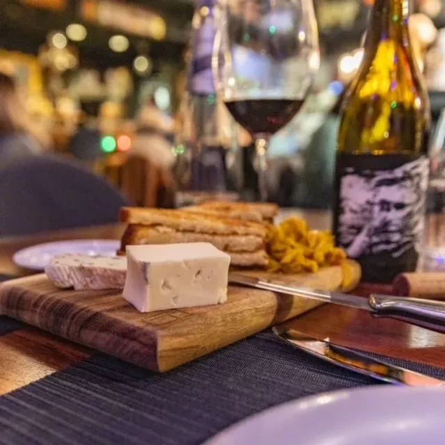 Rustic cheese board with cheeses, bread, relish, and red wine.
