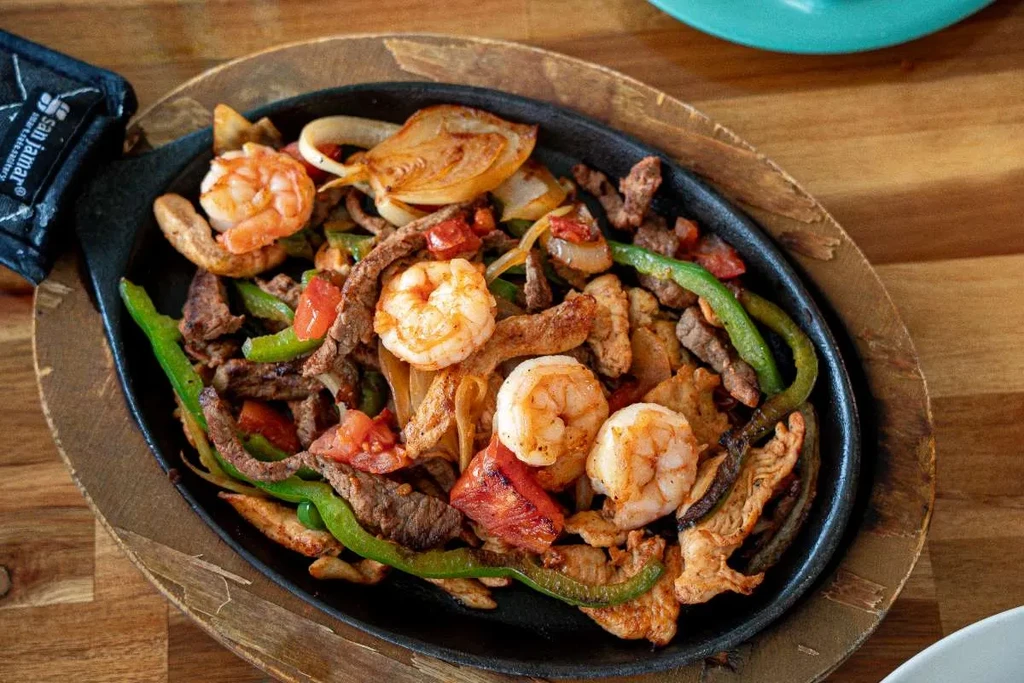 Sizzling cast iron fajitas with shrimp, beef, chicken, and vegetables.