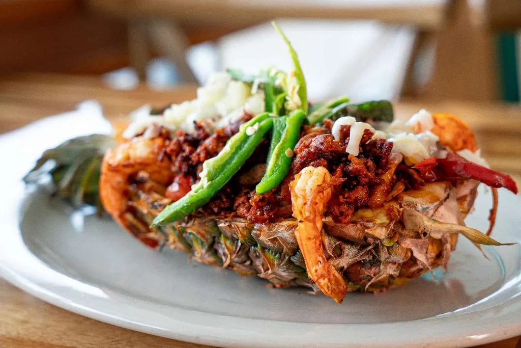 Half grilled pineapple filled with meat, shrimp, chilies, and crumbled cheese.