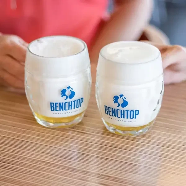 Two Benchtop Craft Brewing beers in barrel glasses on a wooden table.