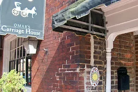 Omar's Carriage House exterior: weathered bricks, green awning, decorative sun tile.