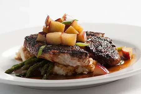 Plated seared protein, diced fruit, mashed potatoes, asparagus, brown sauce.