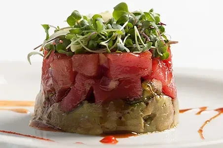 Cylindrical tuna tartare stack with avocado, microgreens, and sauce.