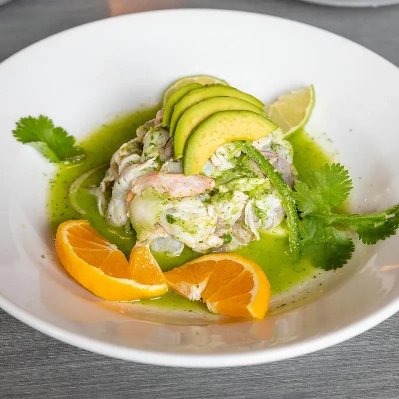 Top-down view of seafood salad with avocado, green sauce, lime, orange.