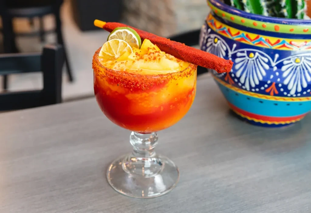 Colorful layered frozen drink with chili-lime rim, lime, and red candy roll.