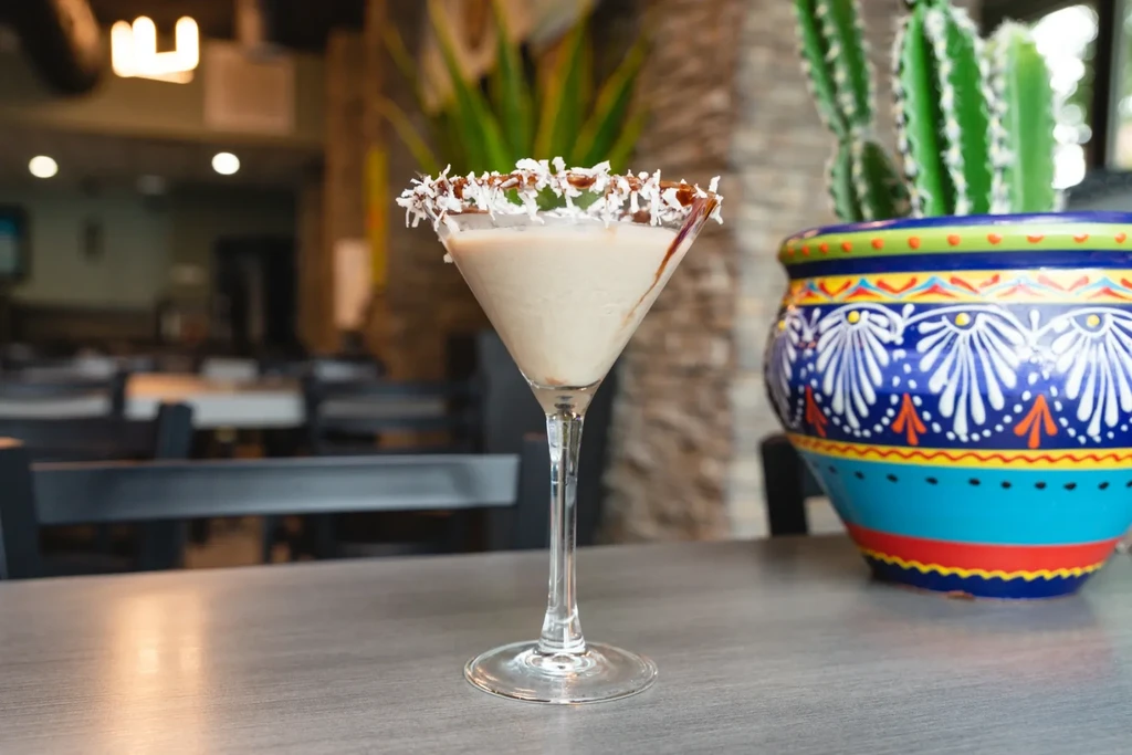 Creamy drink in a martini glass with coconut rim, chocolate, and cactus.