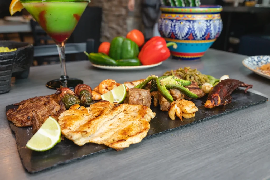 Grilled meat, seafood, and vegetable platter with a layered cocktail.