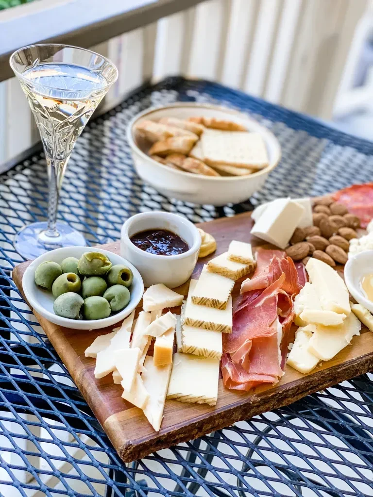 Outdoor charcuterie board with cheeses, meats, olives, and wine.