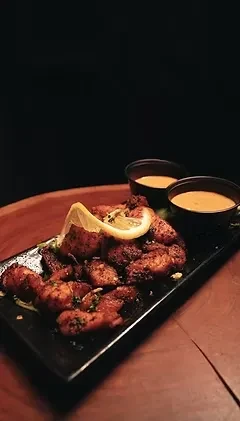 Grilled meat with dark spices, lemon, and sauce on a black plate.