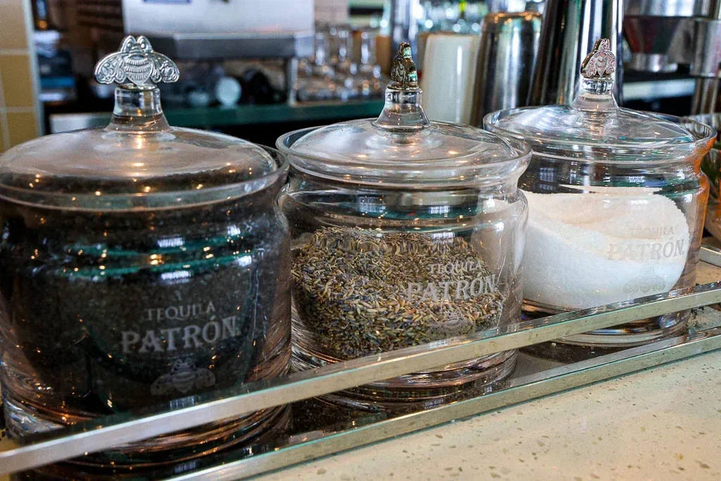 Three Patron jars with black salt, lavender, and white sugar on tray.