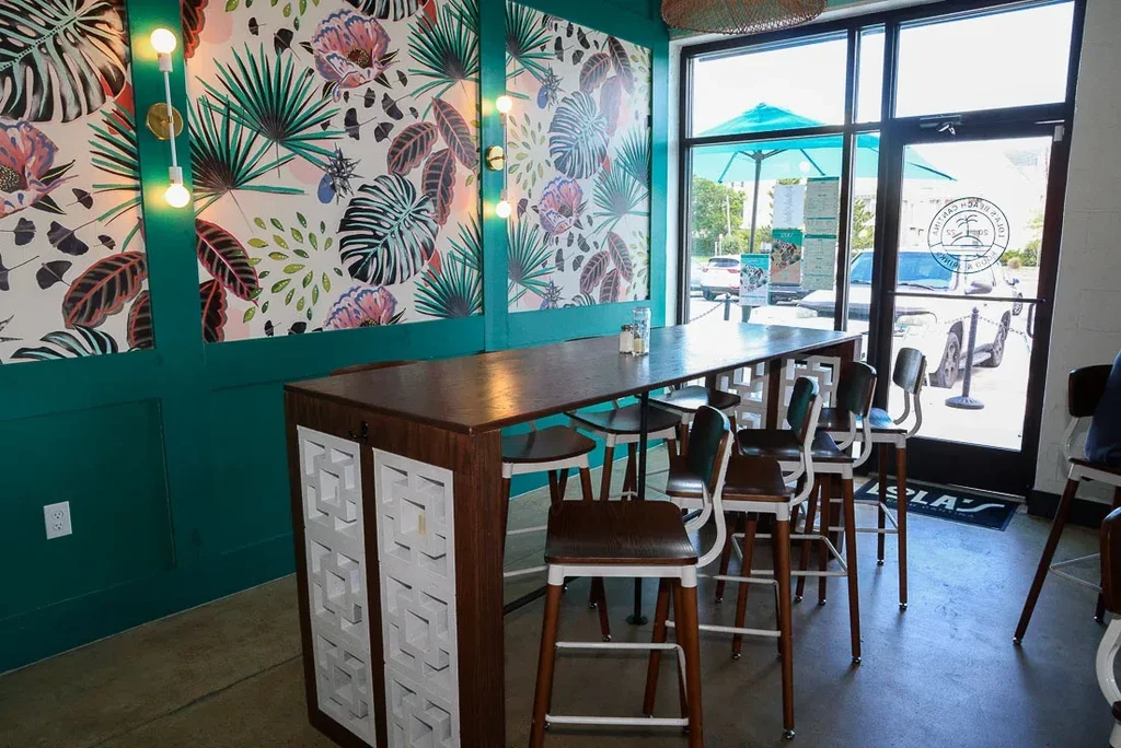 Modern restaurant interior with dark communal table and tropical wallpaper.