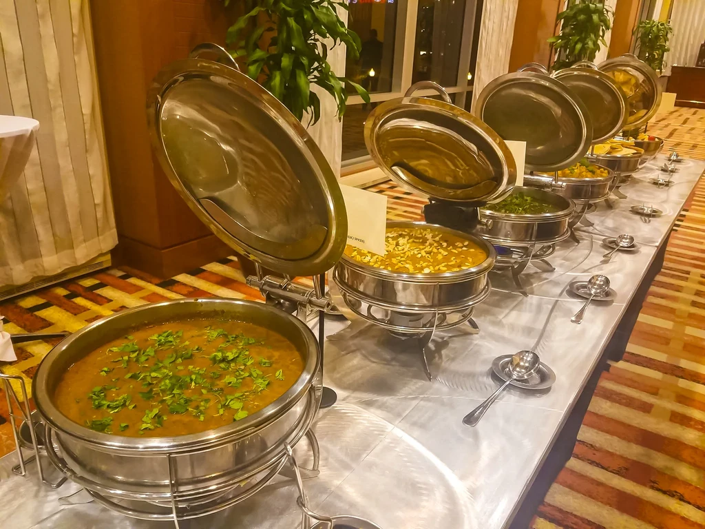 Buffet line of Indian curries and lentils in silver chafing dishes.