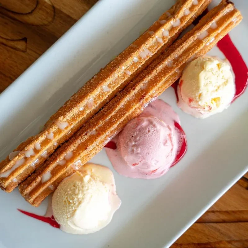 Two cinnamon-sugar churros, three ice cream scoops, and red sauce.