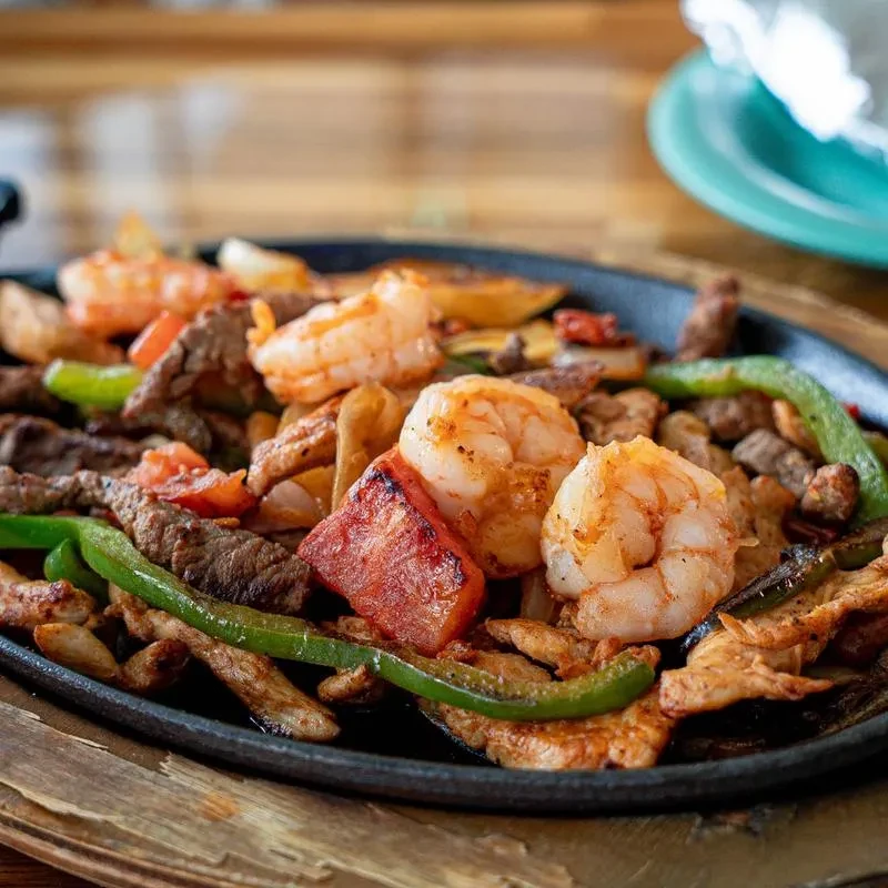 Sizzling skillet of shrimp, beef, chicken fajitas with vegetables.