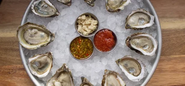 Shucked oysters on ice with three sauces on a silver tray.