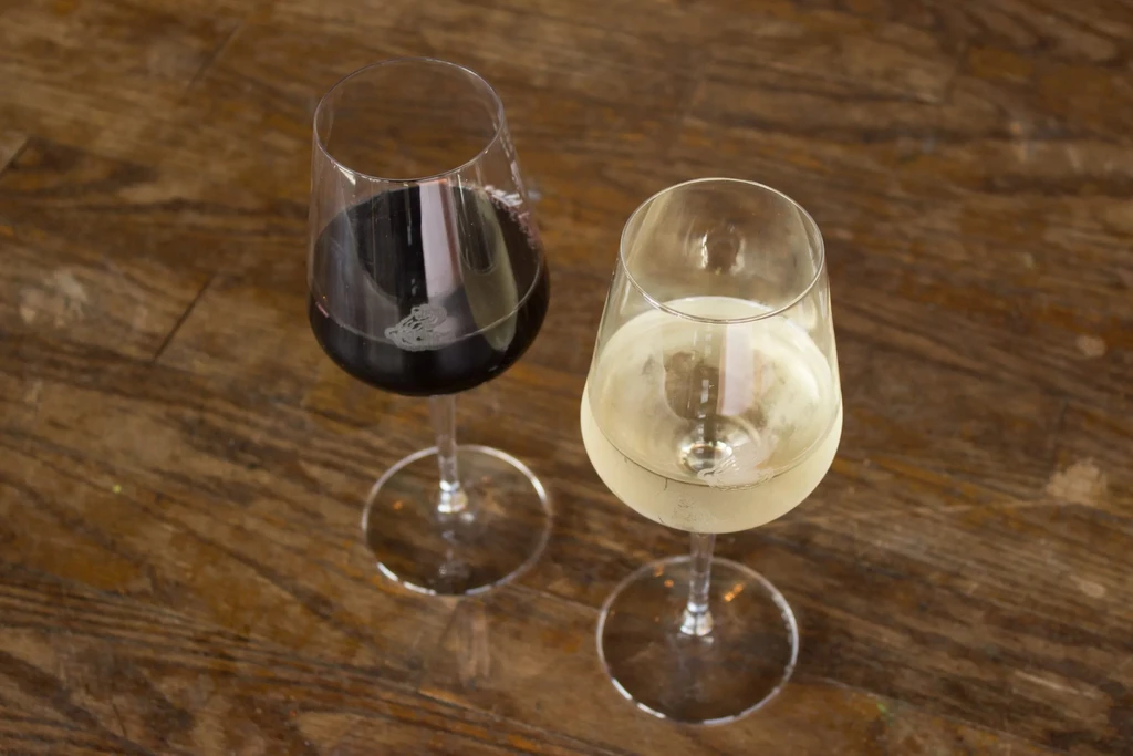 Two wine glasses with red and white wine on rustic wood.