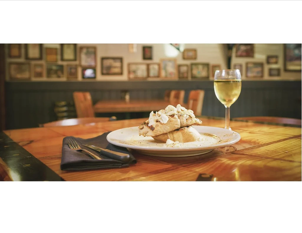 Grilled fish with creamy sauce, white wine, and cutlery on a wooden table.