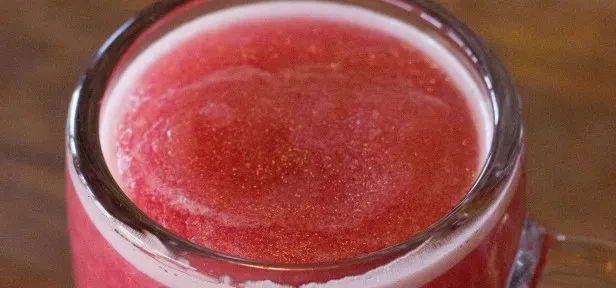 Frothy reddish-pink slushy drink in a clear glass, close-up.