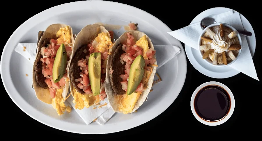 Flat lay of breakfast tacos, banana pudding, and coffee on a black background.