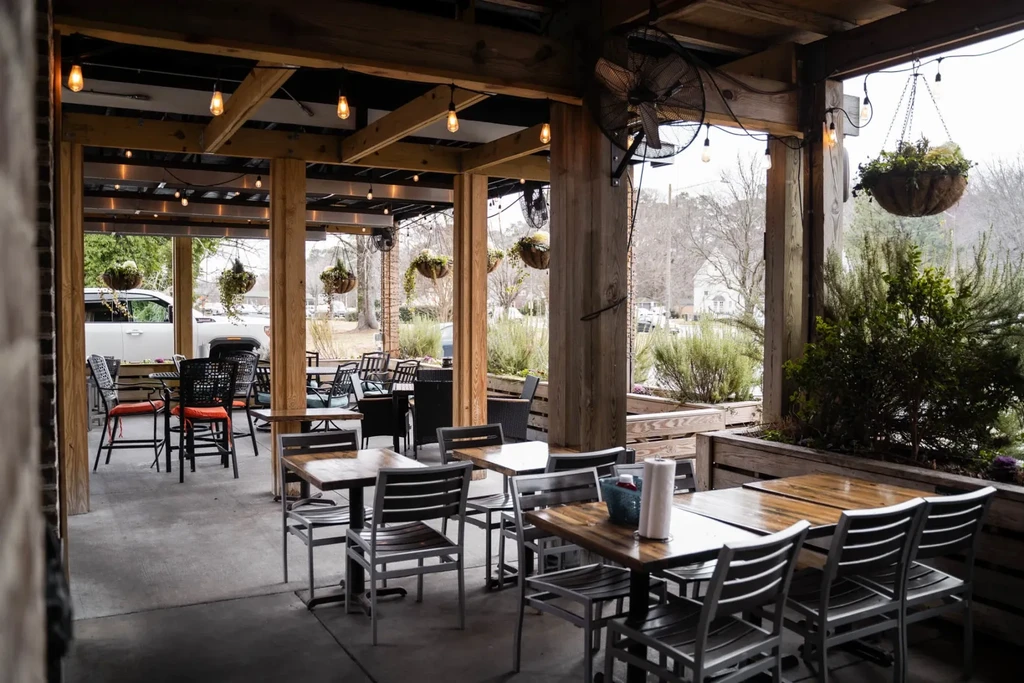 Covered patio dining space with wooden tables, string lights, and plants.