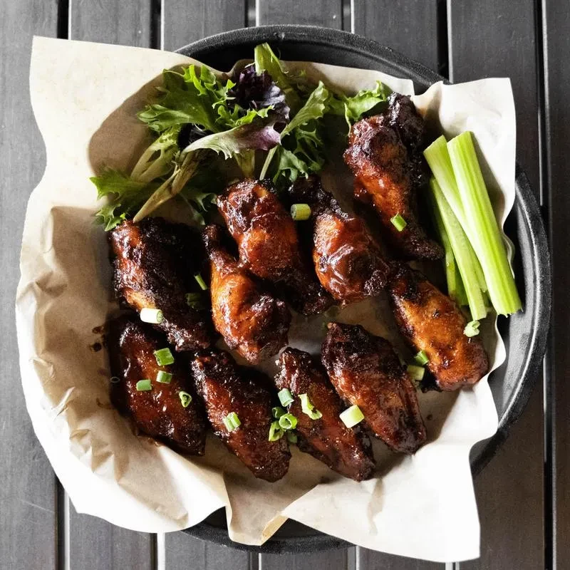 Overhead shot of glossy chicken wings, green onions, lettuce, and celery.