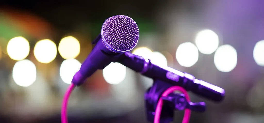 Purple microphone on stand with pink cable against blurred lights.