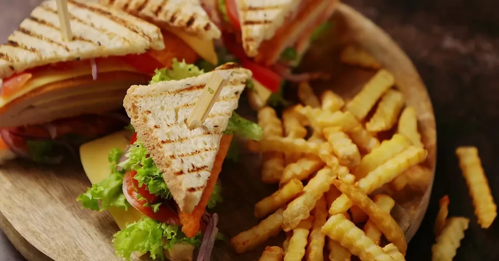 Toasted club sandwiches, layered, with crinkle-cut fries on a wooden board.