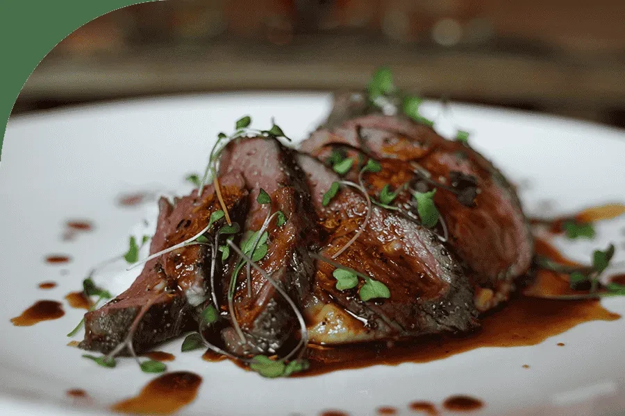 Medium-rare sliced meat, drizzled with sauce and garnished with microgreens.