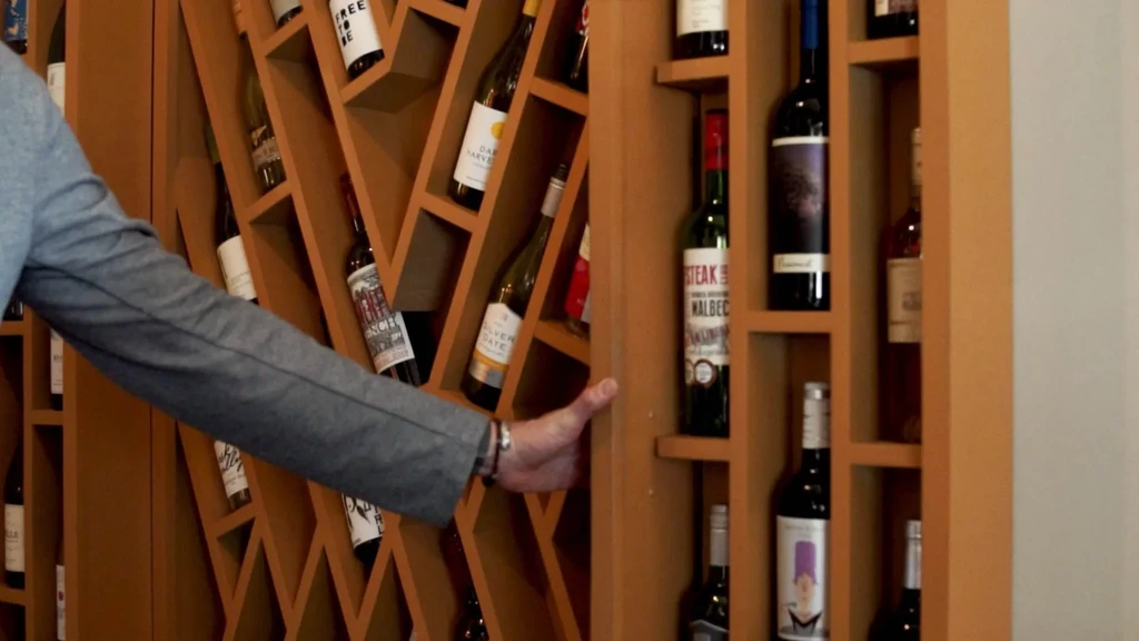 Modern wooden wine rack filled with bottles, hand touching wood.