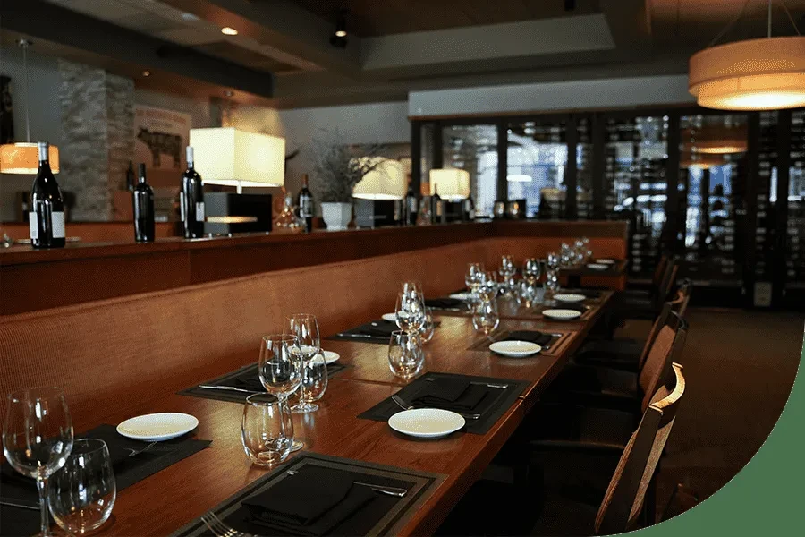 Elegant restaurant interior with long set dining table and wine cellar.