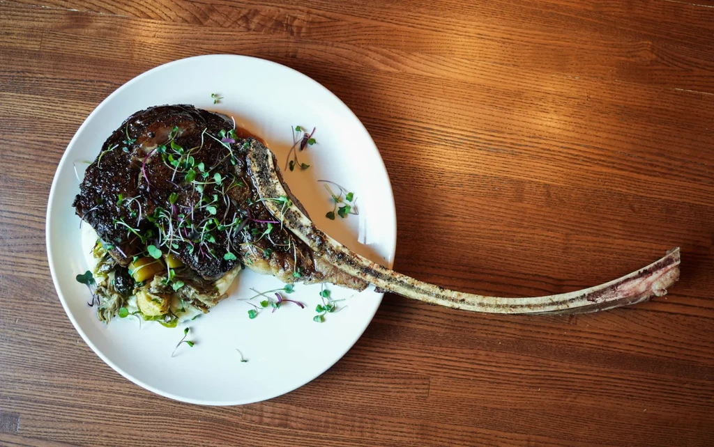 Seared tomahawk steak with mashed potatoes, vegetables, and microgreens.