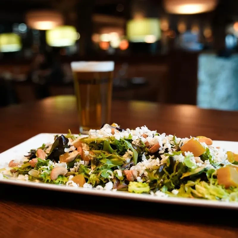 Fresh mixed greens salad with cheese, nuts, and fruit, beside a beer.