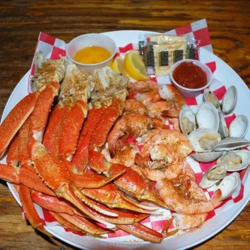 Seafood platter with crab legs, shrimp, clams, sauces, and lemon.