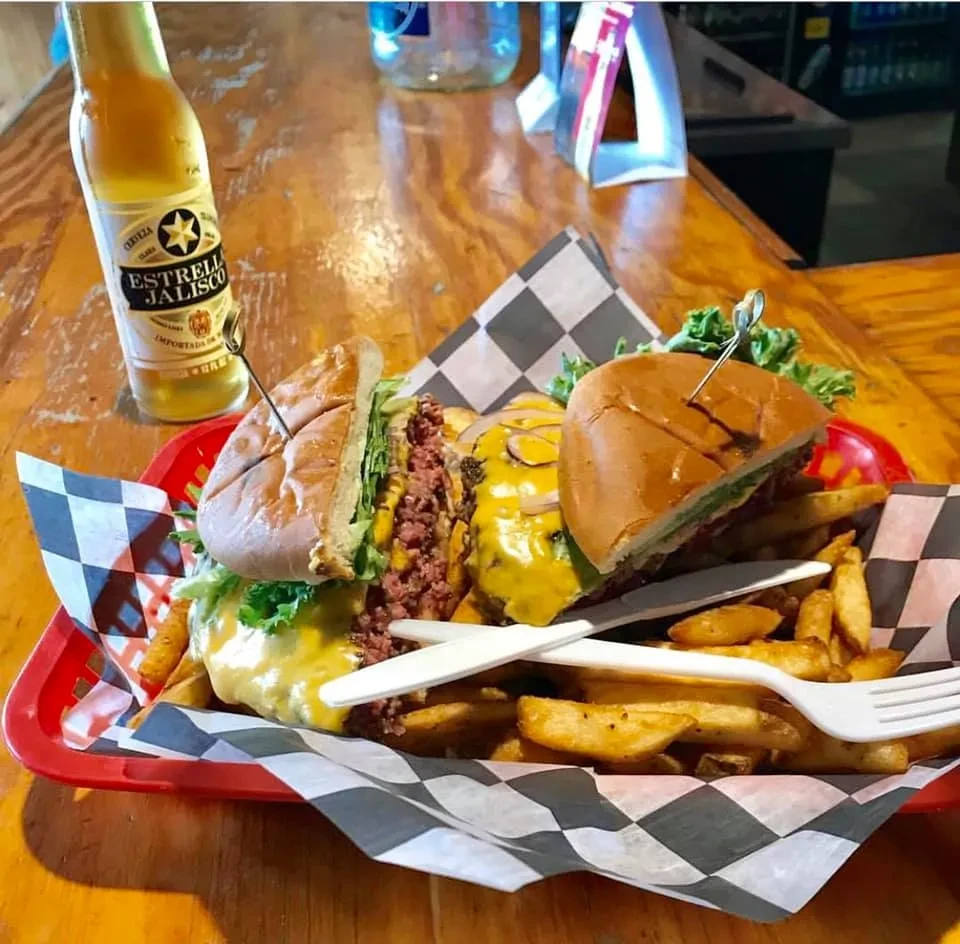 Red basket with two burgers, fries, and Estrella Jalisco beer.