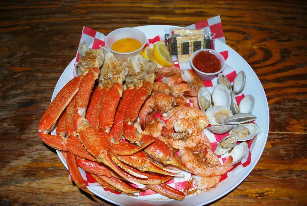 Platter with snow crab legs, shrimp, clams, butter, and cocktail sauce.